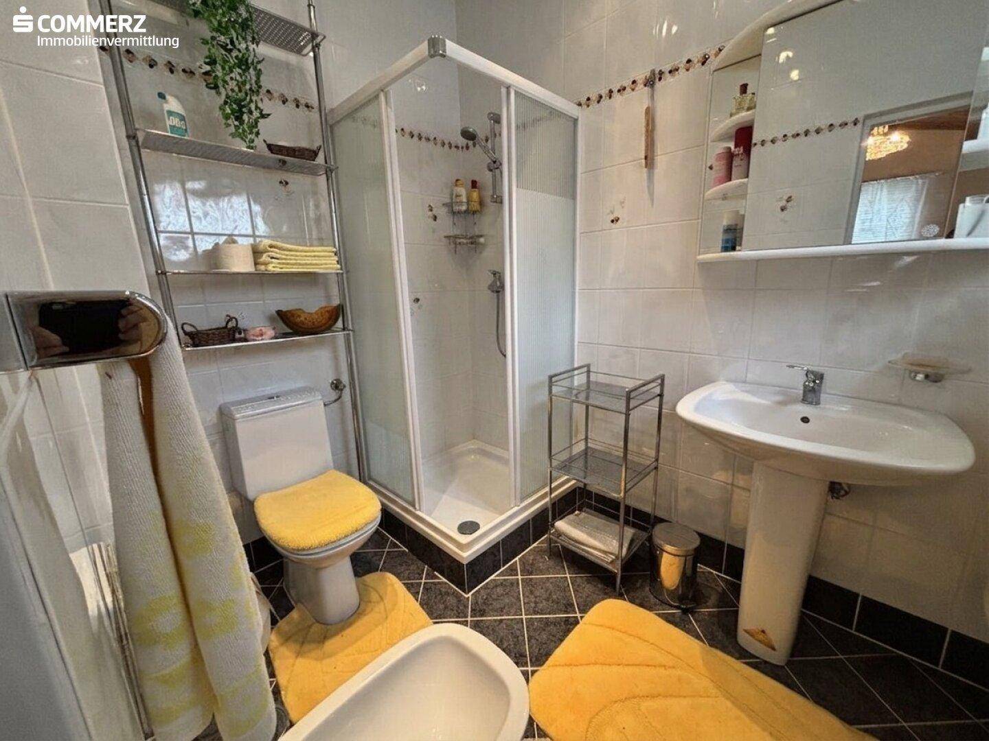 Badezimmer mit Duschkabine, WC, Waschbecken und kontrastreichen Schwarz-Weiß-Fliesen.
