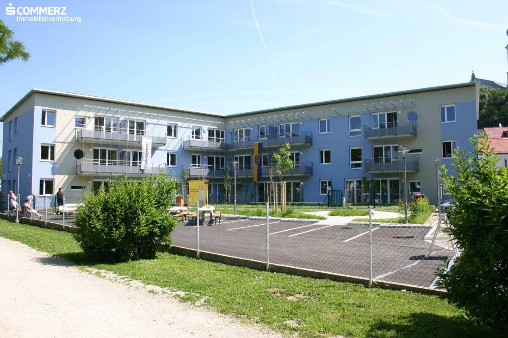 Modernes Mehrfamilienhaus mit blauer Fassade, Balkonen und Außenparkplätzen.