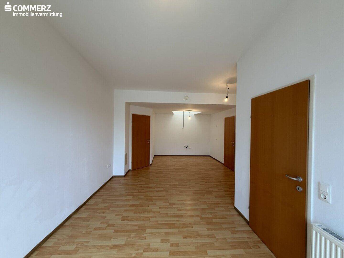 Geräumiger, unmöblierter Innenraum mit hellem Laminatboden und weißen Wänden.