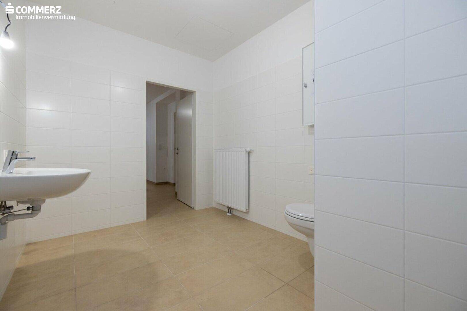 Funktionales Badezimmer mit Waschbecken, WC und Heizkörper, hell gefliest.