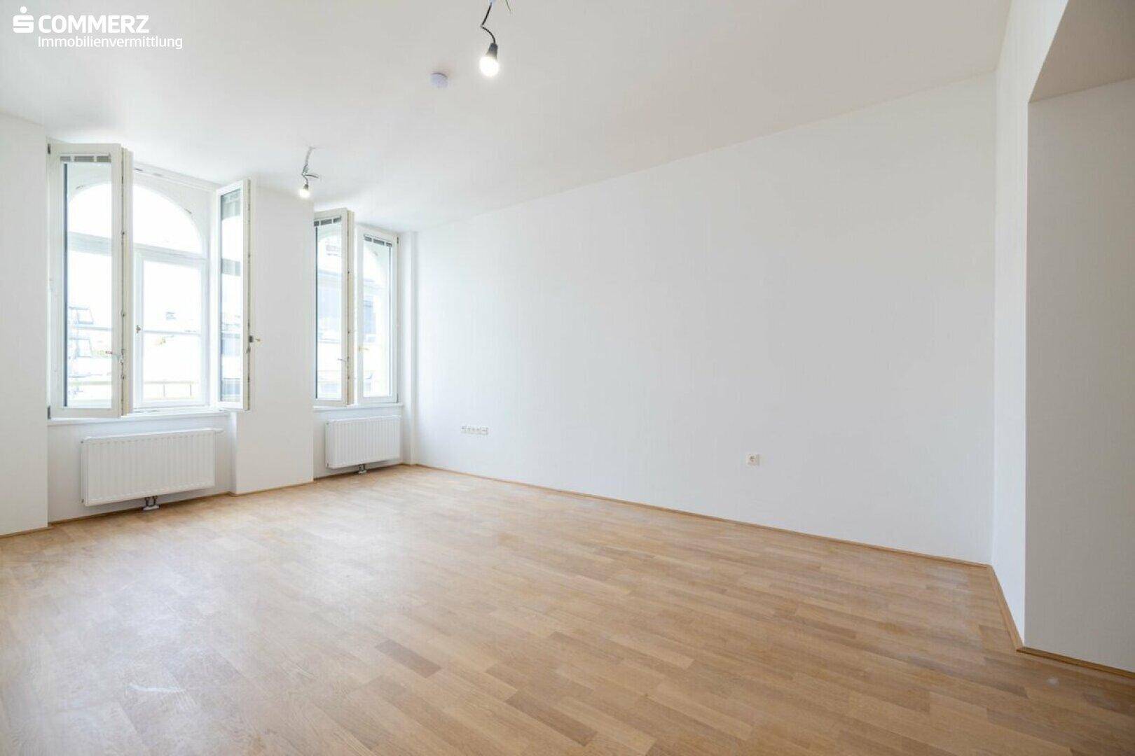 Heller, leerer Raum mit eleganten Bogenfenstern und hellem Parkettboden.