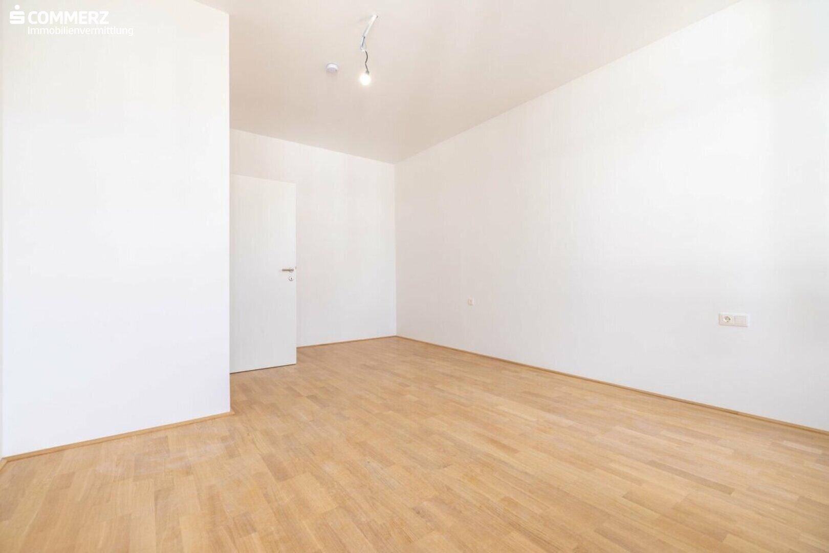 Leeres Zimmer mit hellem Parkettboden und weißer Tür, bereit zur Einrichtung.