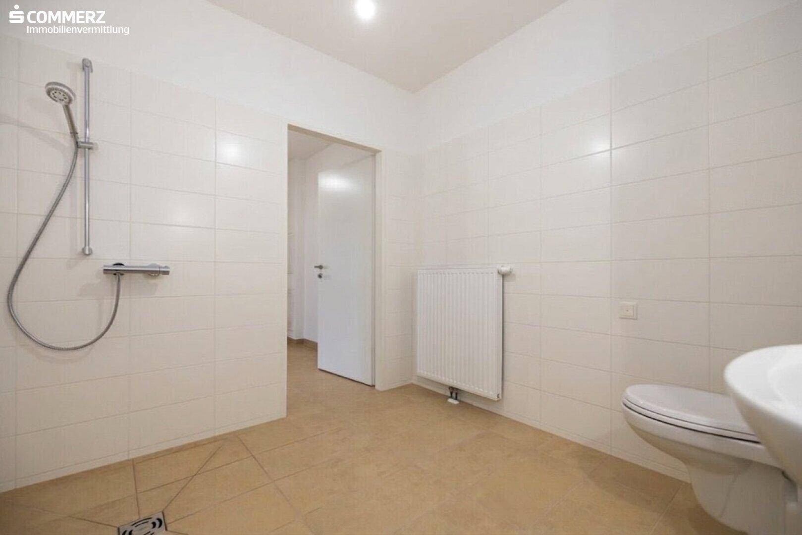 Helles Badezimmer mit weißen Fliesen, Dusche und WC, funktional und sauber.