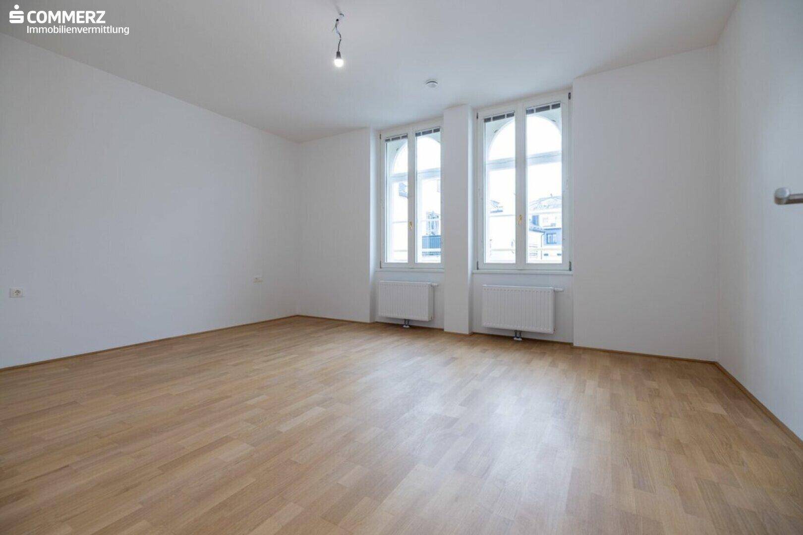 Heller Raum mit Parkettboden und eleganten Bogenfenstern, bietet viel Tageslicht.
