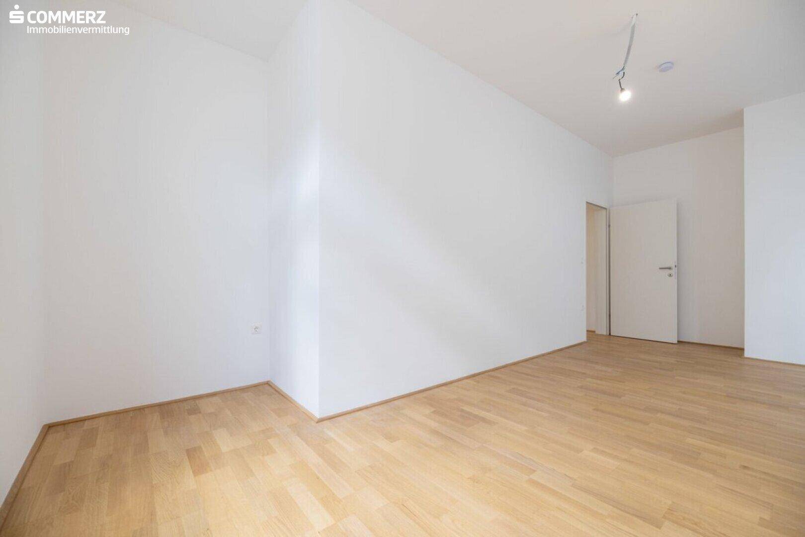 Schlichter, leerer Raum mit Parkettboden und weißen Wänden, vielseitig nutzbar.
