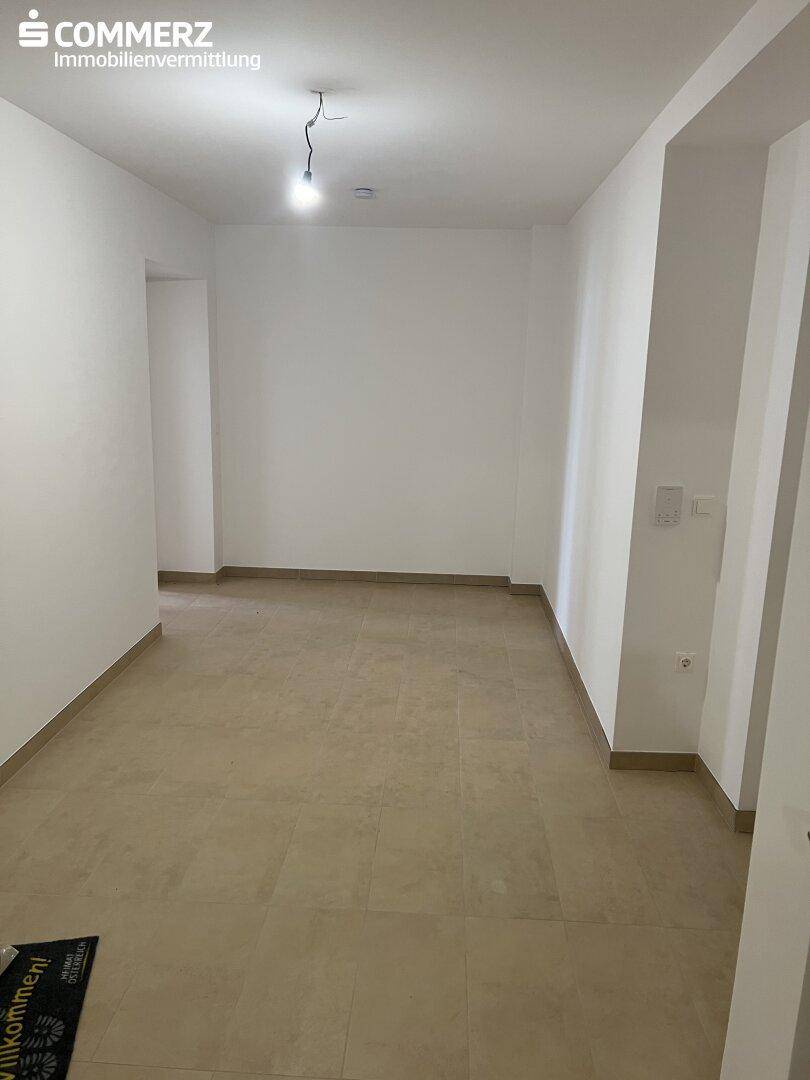 Heller, leerer Raum mit beigefarbenen Fliesen und weißen Wänden.