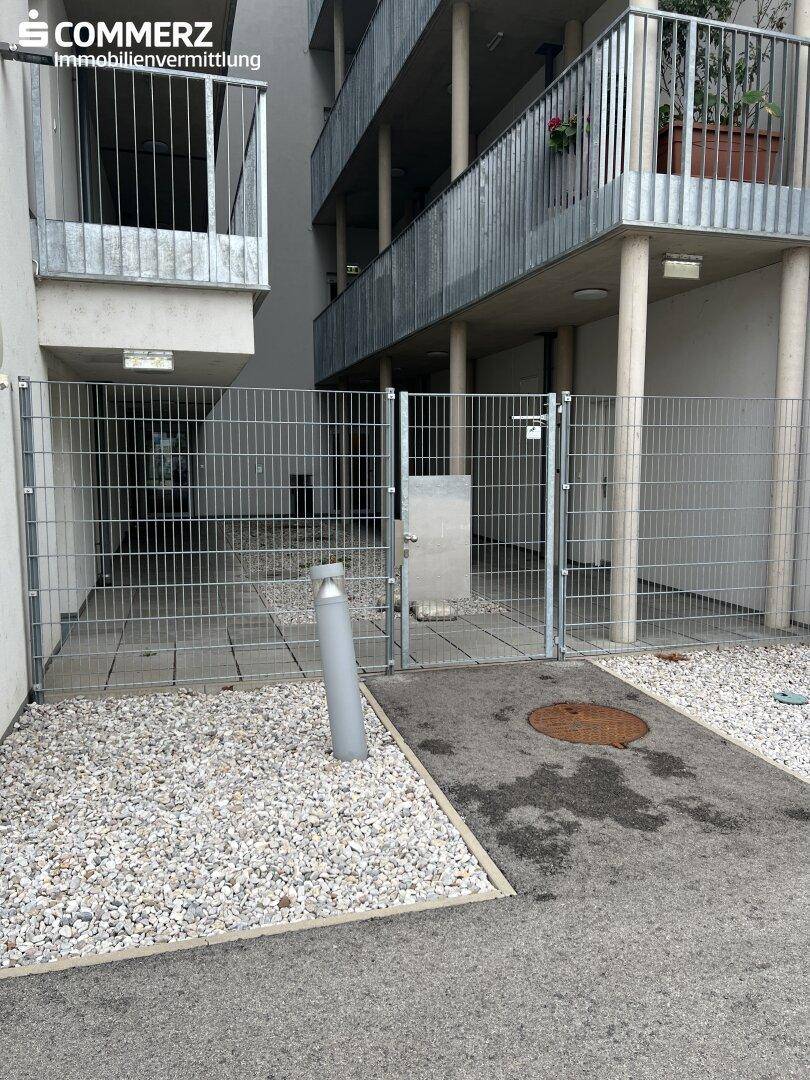 Außenbereich mit Metallzaun, Kiesfläche und Blick auf die Balkone des Gebäudes.