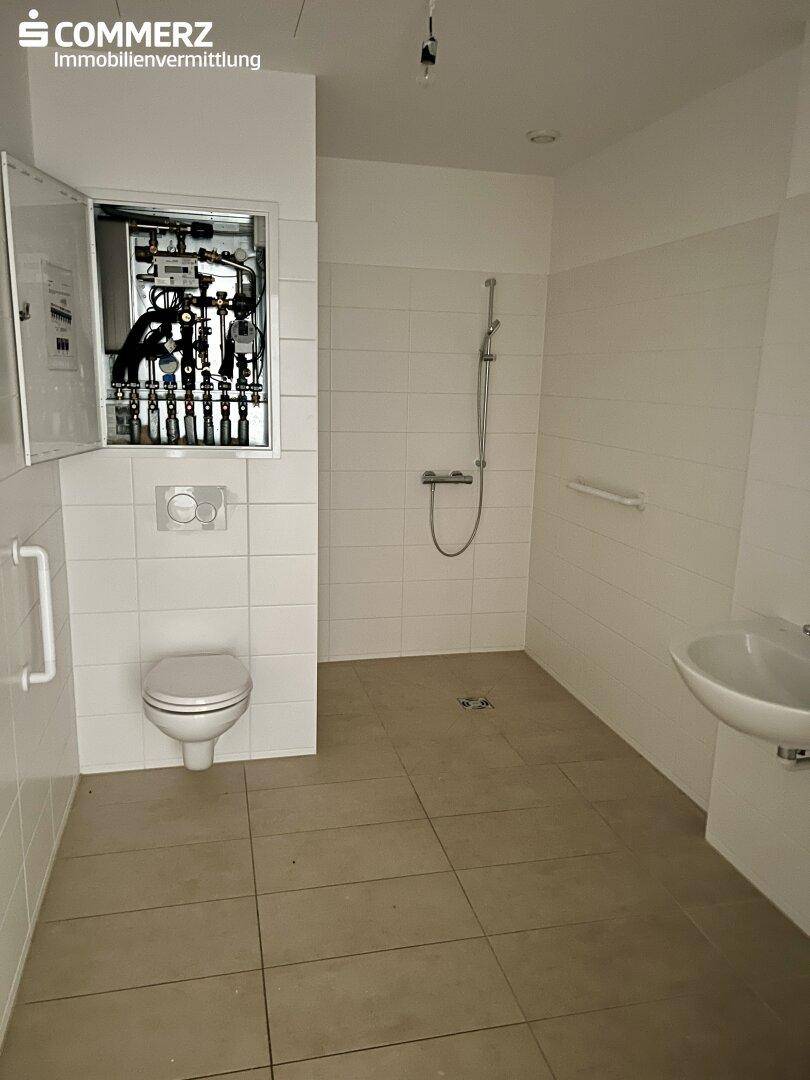 Modernes Badezimmer mit ebenerdiger Dusche, Wand-WC und Haltegriffen für Barrierefreiheit.