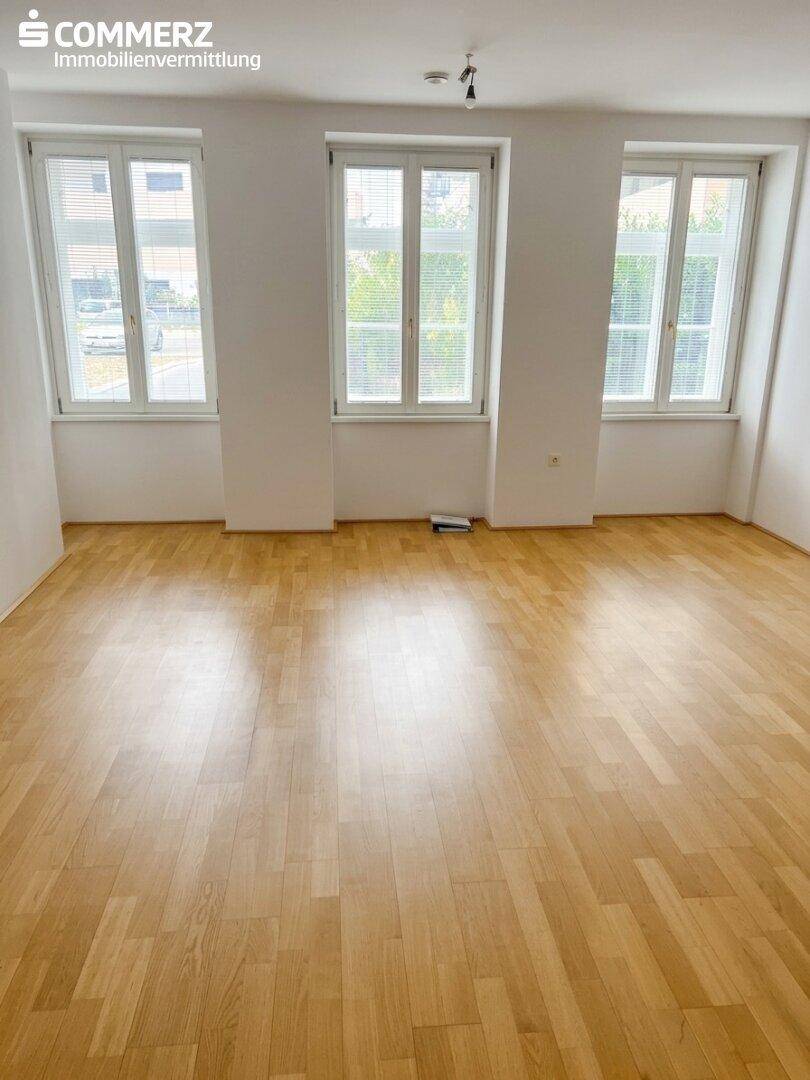 Heller Wohnraum mit klassischem Parkettboden und drei großen Fenstern für viel Tageslicht.