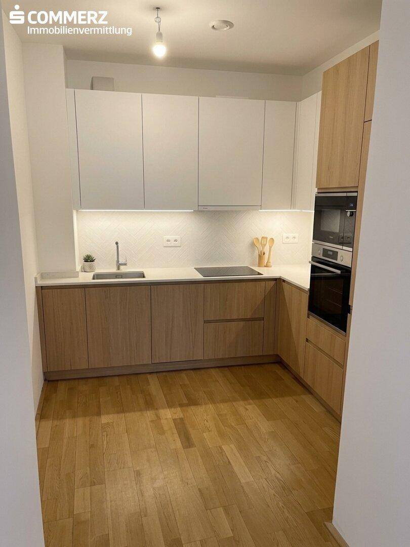 Moderne Einbauküche mit hellen Holzfronten, weißen Oberschränken und integrierten Elektrogeräten.