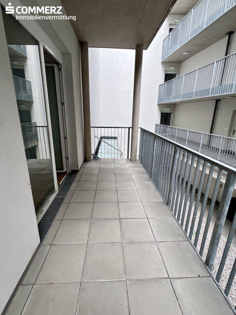 Langer, gefliester Balkon mit Metallgeländer und Blick auf den Innenhof des Gebäudes.