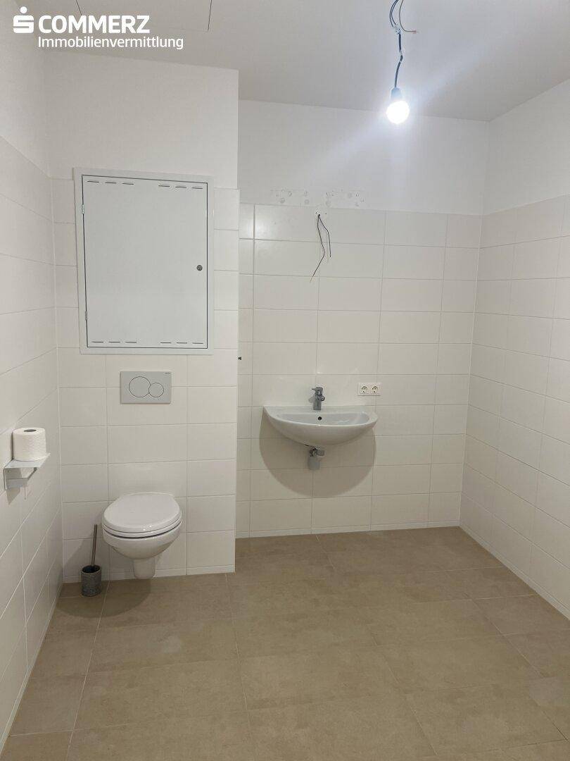 Modernes Gäste-WC mit Wand-WC, Waschbecken und hellen Fliesen, unmöbliert.