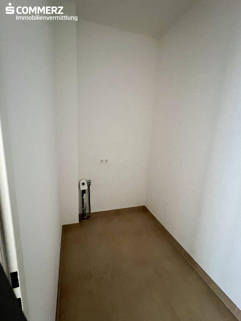 Kleiner Abstellraum mit Anschlüssen und Fliesenboden, ideal für Waschmaschine oder Lagerung.