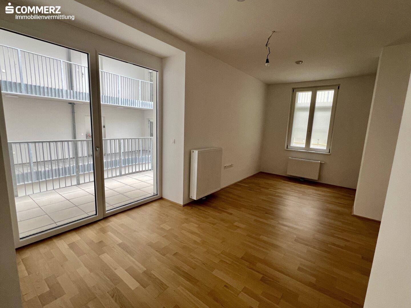 Geräumiges, leeres Wohnzimmer mit Holzboden und großen Fenstern, bereit zur individuellen Gestaltung.