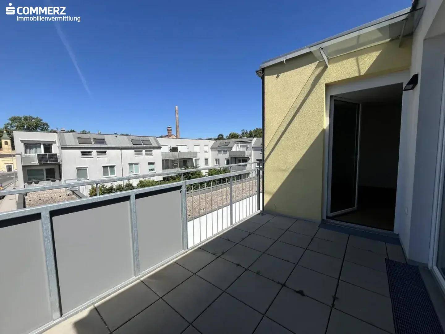 Geräumiger, leerer Balkon mit Fliesenboden und Blick auf die Nachbarschaft unter blauem Himmel.