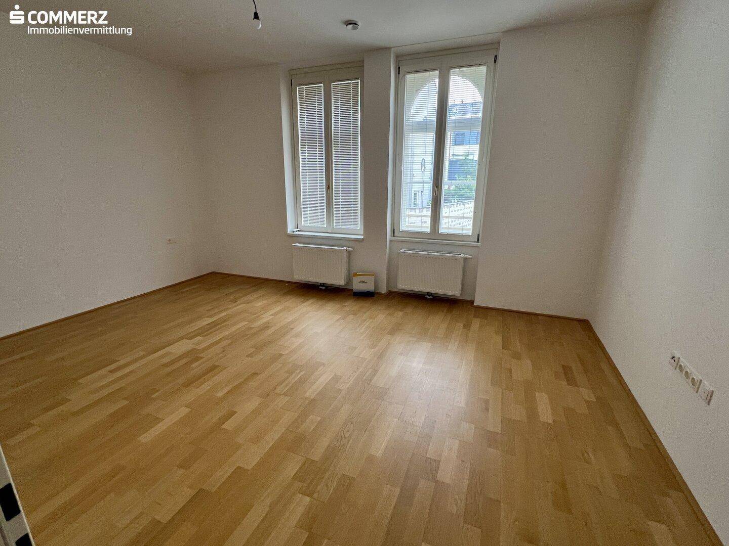 Heller, unmöblierter Raum mit Holzboden und zwei hohen Fenstern, ideal für Schlaf- oder Wohnbereich.