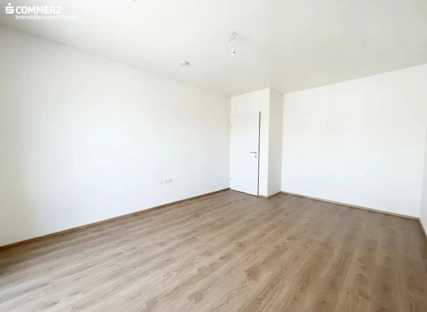 Helles, leeres Zimmer mit Holzboden und weißen Wänden, vielseitig nutzbar als Schlaf- oder Arbeitszimmer.