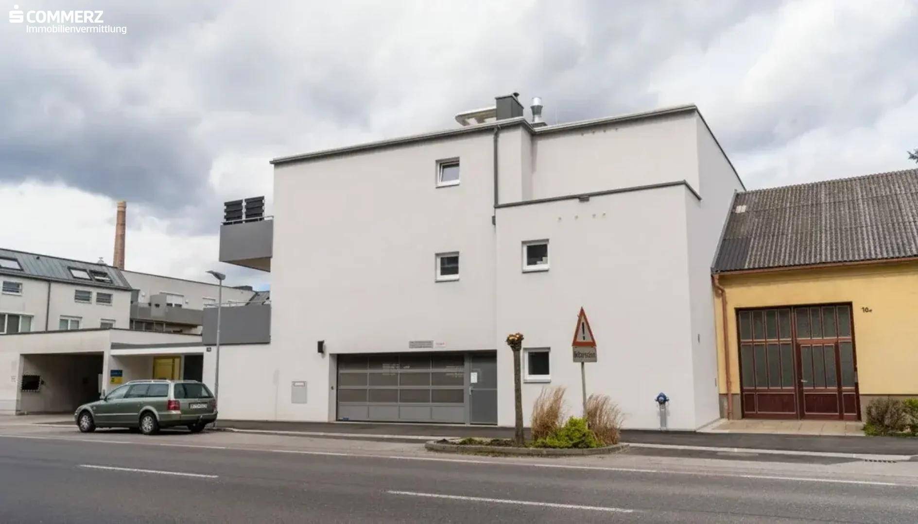 Gebäudeansicht von der Straße mit Garagen und moderner Architektur unter bewölktem Himmel.