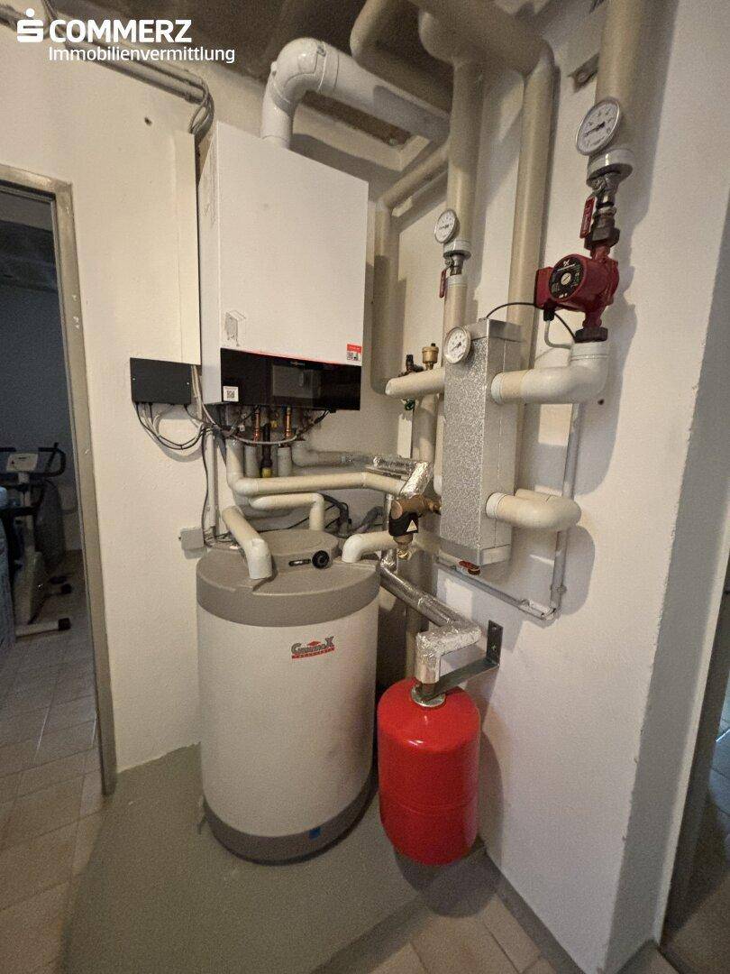 Heizungsraum mit moderner Heizungsanlage und Warmwasserspeicher im Kellerbereich.