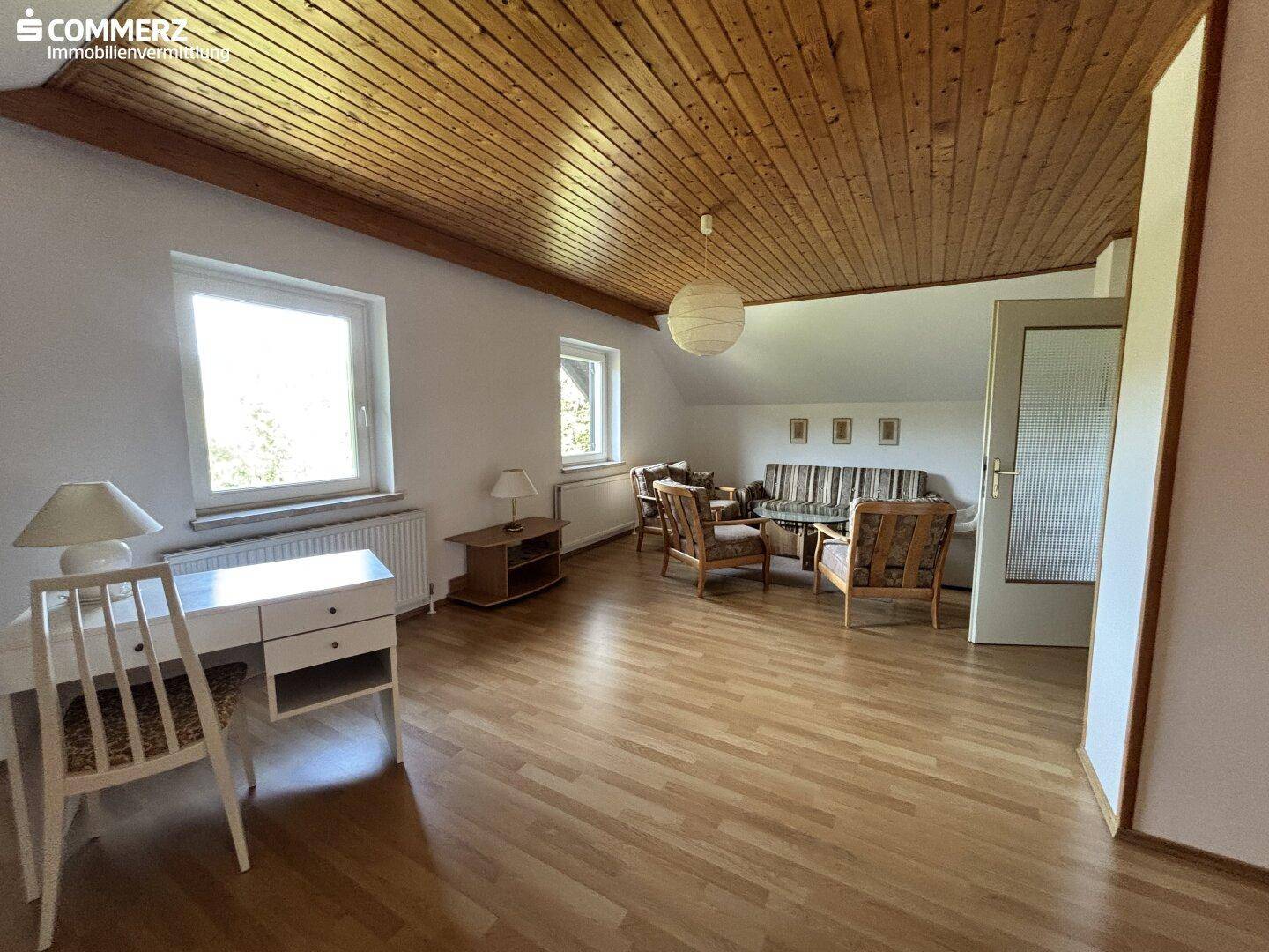 Heller Wohnraum mit Holzbalkendecke, Parkettboden und Sitzgelegenheiten.