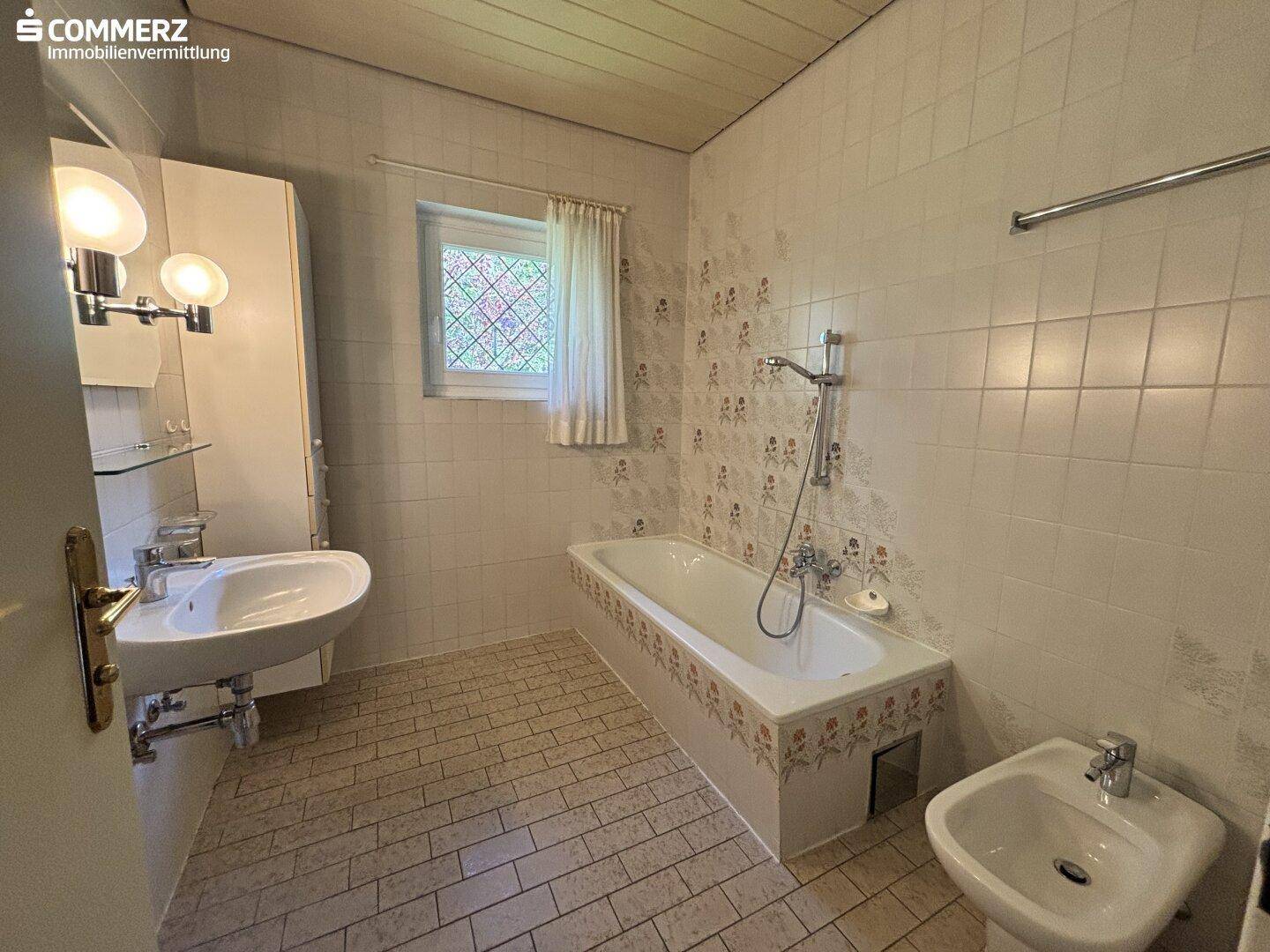 Badezimmer mit Badewanne, Waschbecken, Bidet und Fenster, ausgestattet mit Fliesen.