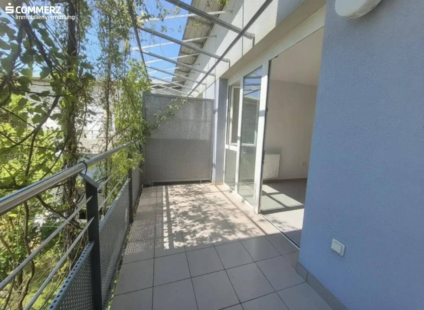 Heller Balkon mit Fliesenboden, Metallgeländer und direktem Zugang zu einem Innenraum.