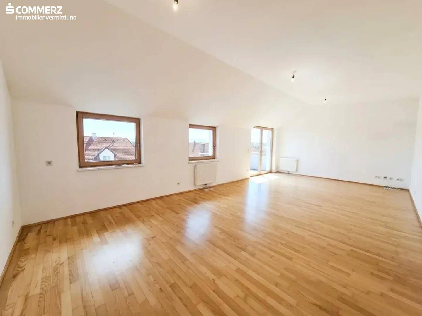 Lichtdurchfluteter Wohnbereich mit Holzboden, Dachschrägen und Blick ins Grüne.