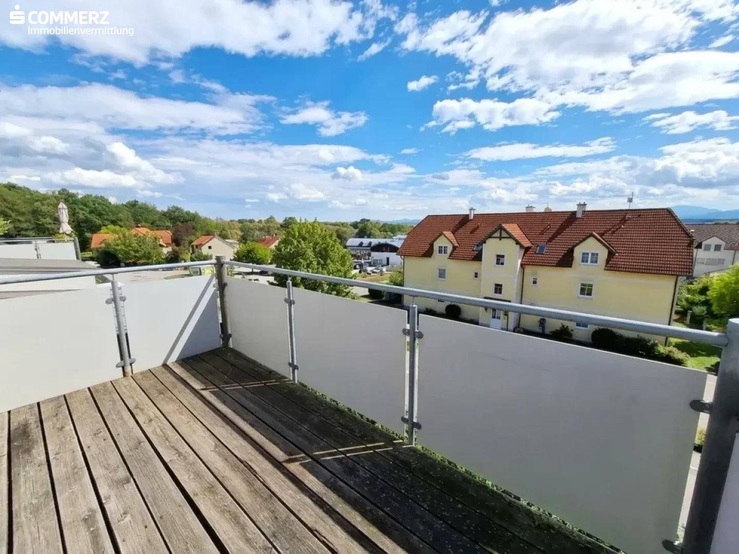 Sonniger Balkon mit Holzboden und weitem Blick über die Dächer der Nachbarschaft.