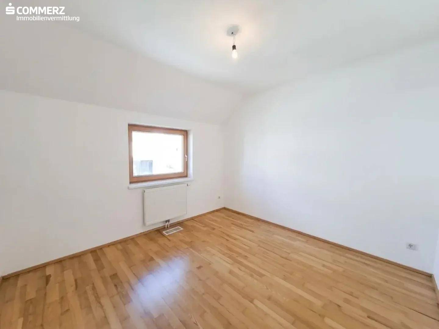 Gemütliches Schlafzimmer mit Holzboden, weiß gestrichenen Wänden und einem Fenster.