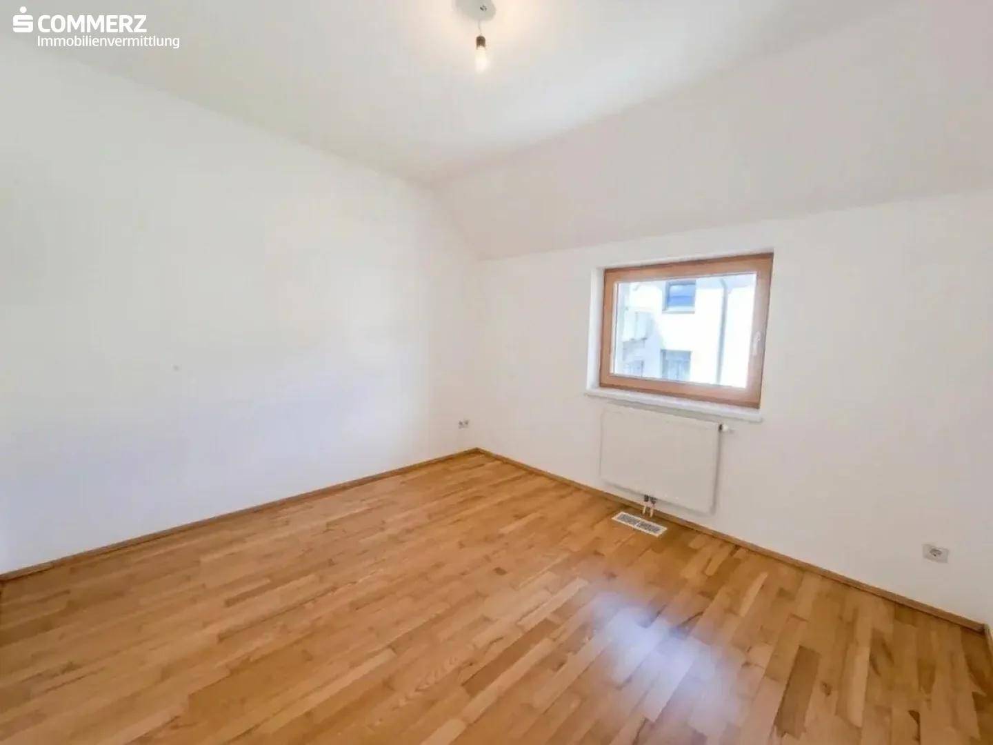 Helles Schlafzimmer mit Holzboden und einem Fenster, das viel Tageslicht hereinlässt.