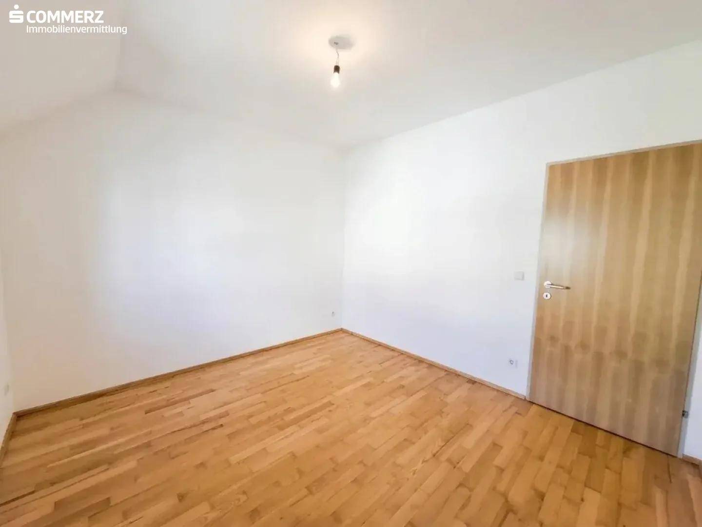 Geräumiges Schlafzimmer mit Holzboden und einer Holztür, bereit zur individuellen Gestaltung.