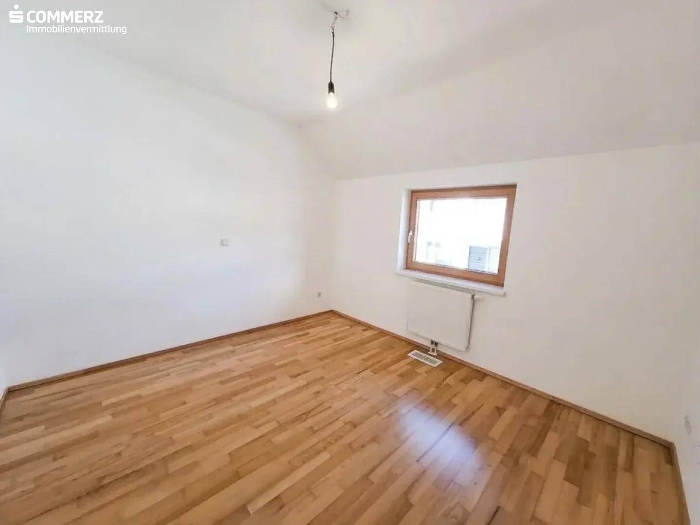 Helles Schlafzimmer mit Holzboden und Fenster, ideal für ein Kinder- oder Gästezimmer.