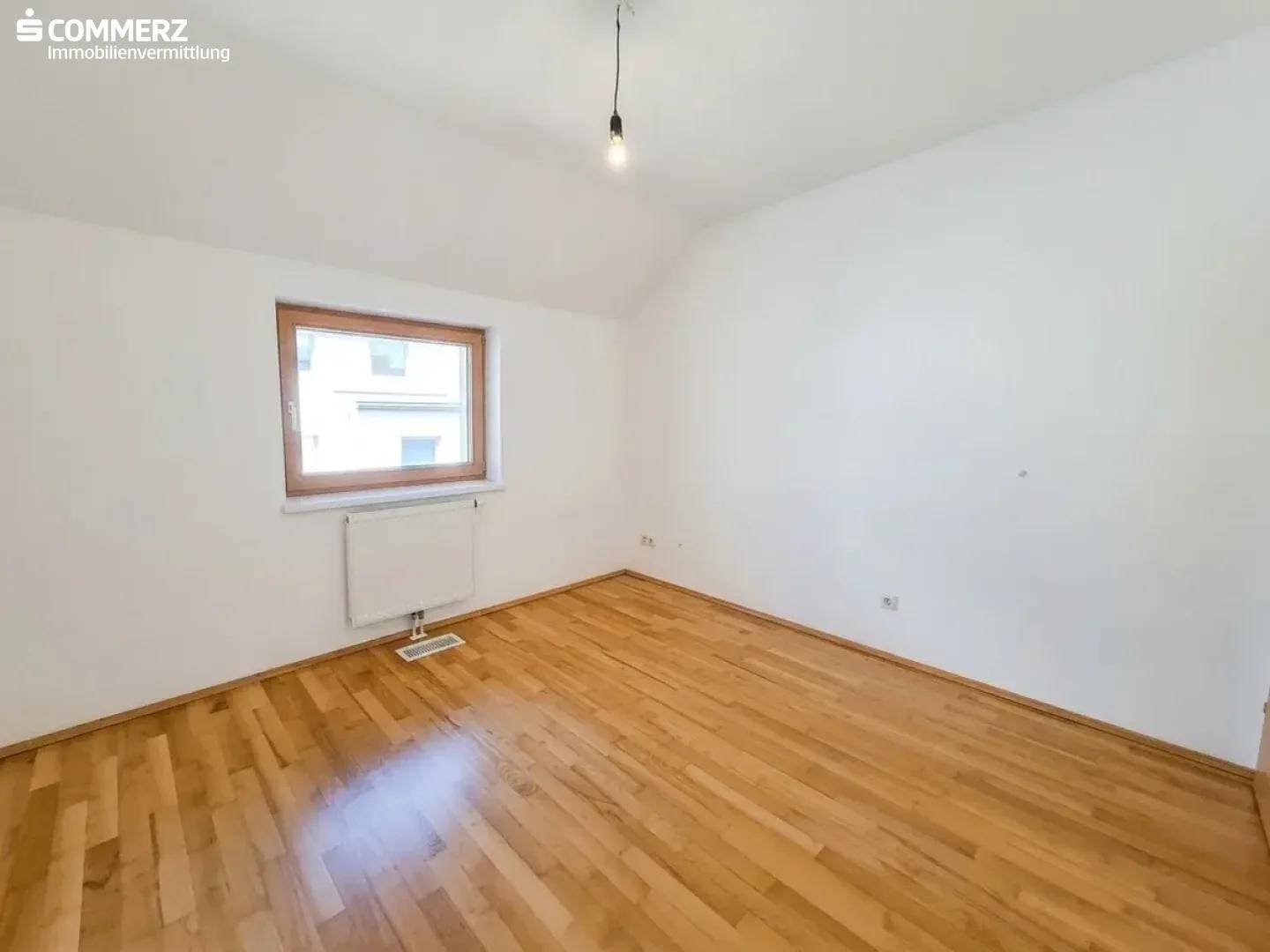 Helles Schlafzimmer mit Holzboden und Fenster, das viel Tageslicht in den Raum bringt.