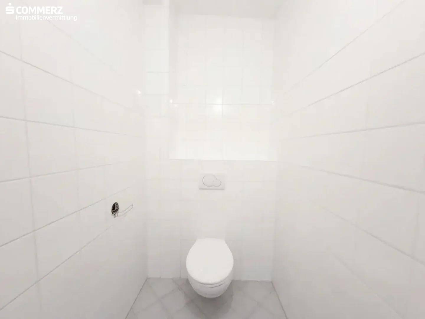 Separates WC mit wandhängender Toilette und weißen Fliesen, funktional und sauber.