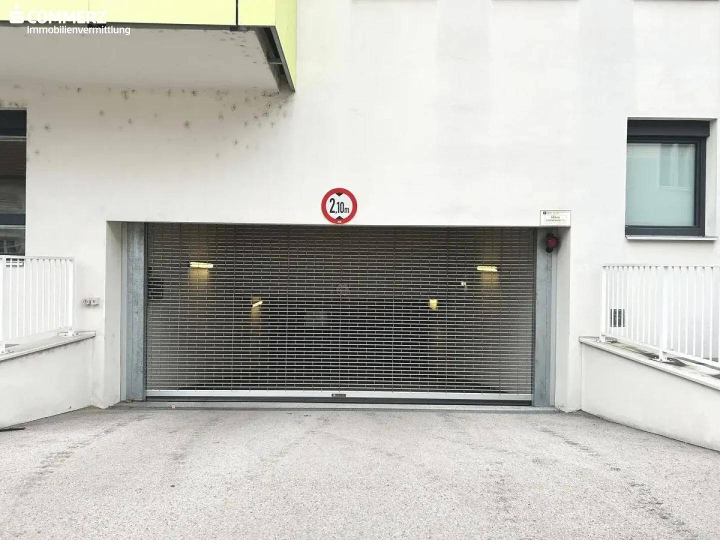 Außenansicht der Tiefgarageneinfahrt mit Rolltor und Höhenbegrenzung von 2,10 Metern, Teil eines Neubaus.