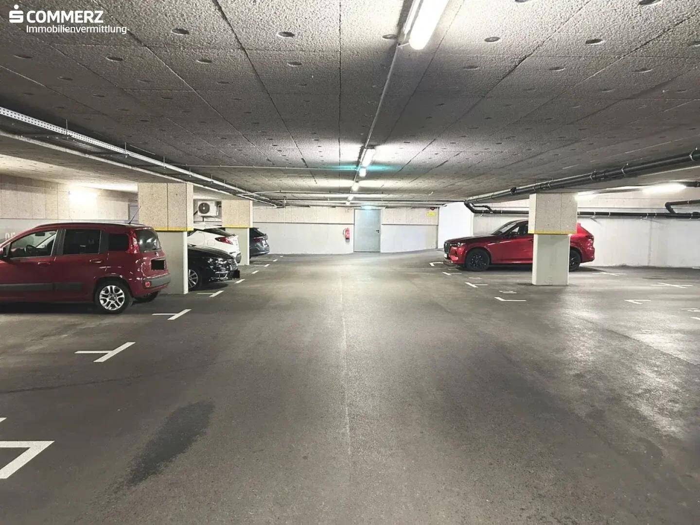 Weitere Ansicht der Tiefgarage mit markierten Parkplätzen und geparkten Fahrzeugen, in gutem Zustand.