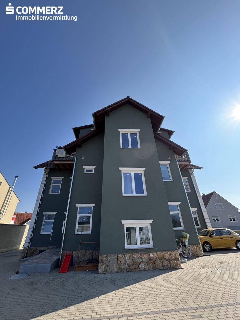 Mehrstöckiges Gebäude mit dunkelgrauer Fassade, weißen Fenstern und Satteldach unter blauem Himmel.