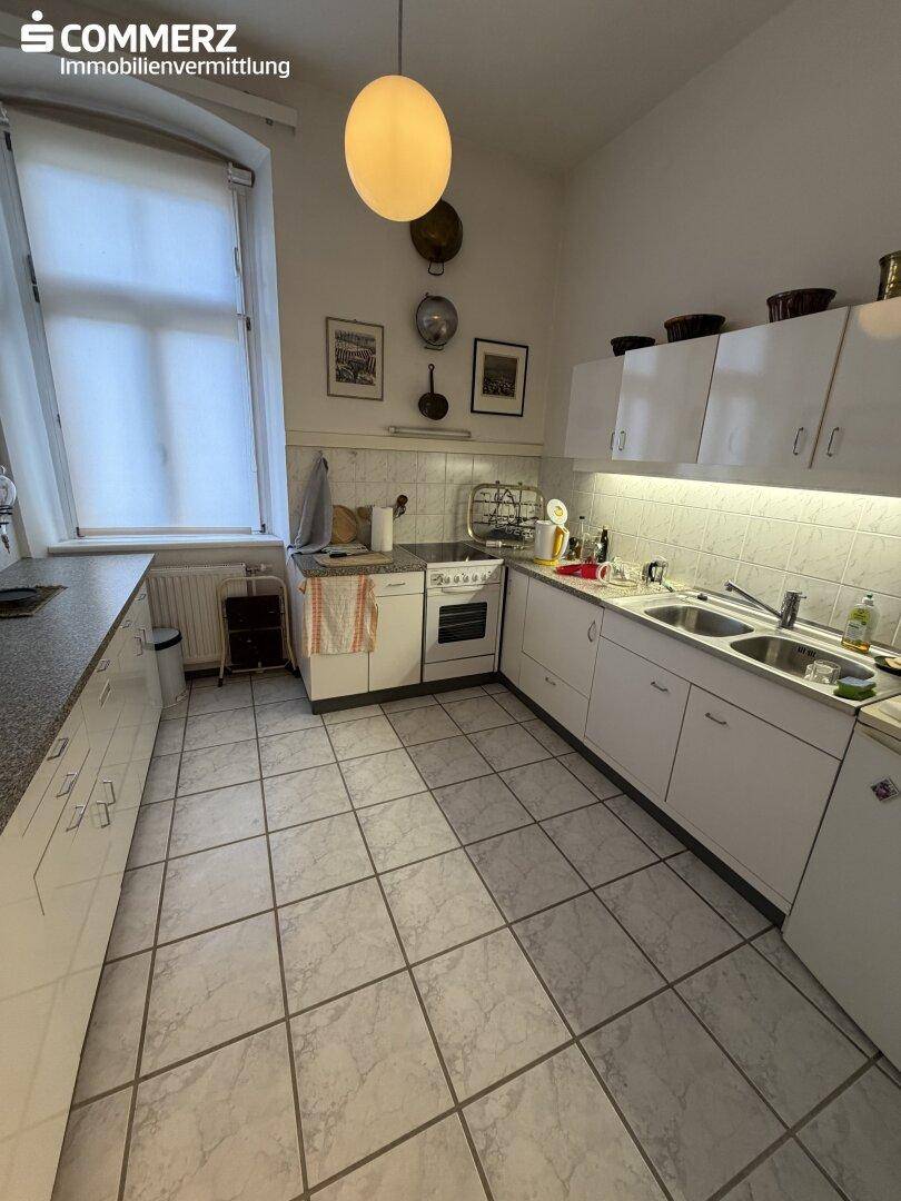 Funktionale Küche mit weißen Schränken, Fliesenboden und Fenster für Tageslicht.