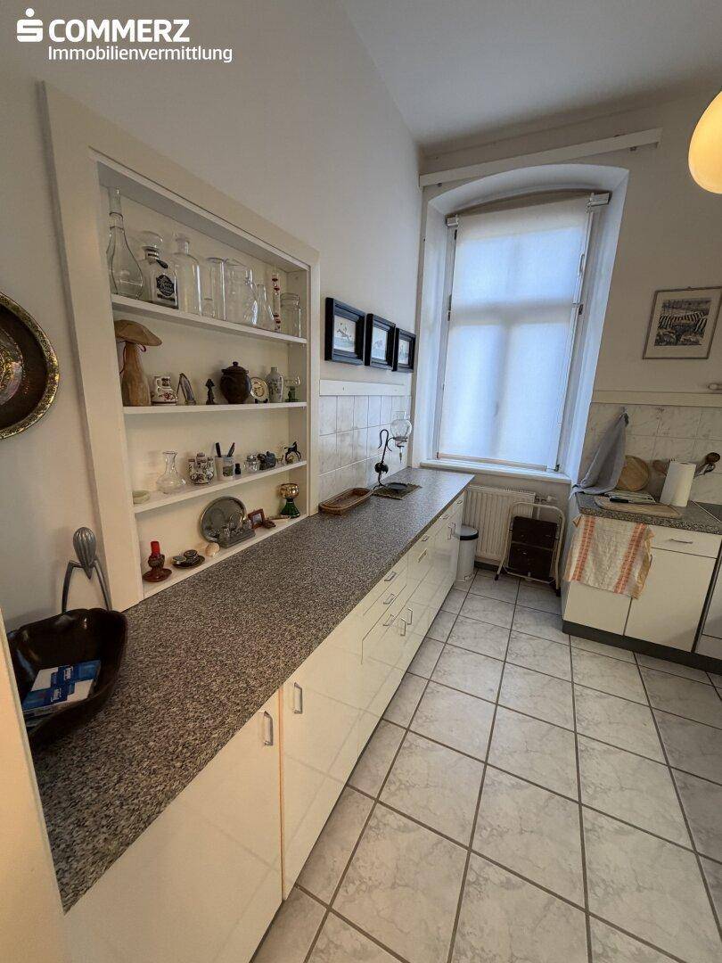 Helle Küche mit weißen Unterschränken, Granitarbeitsplatte und offenem Regal.