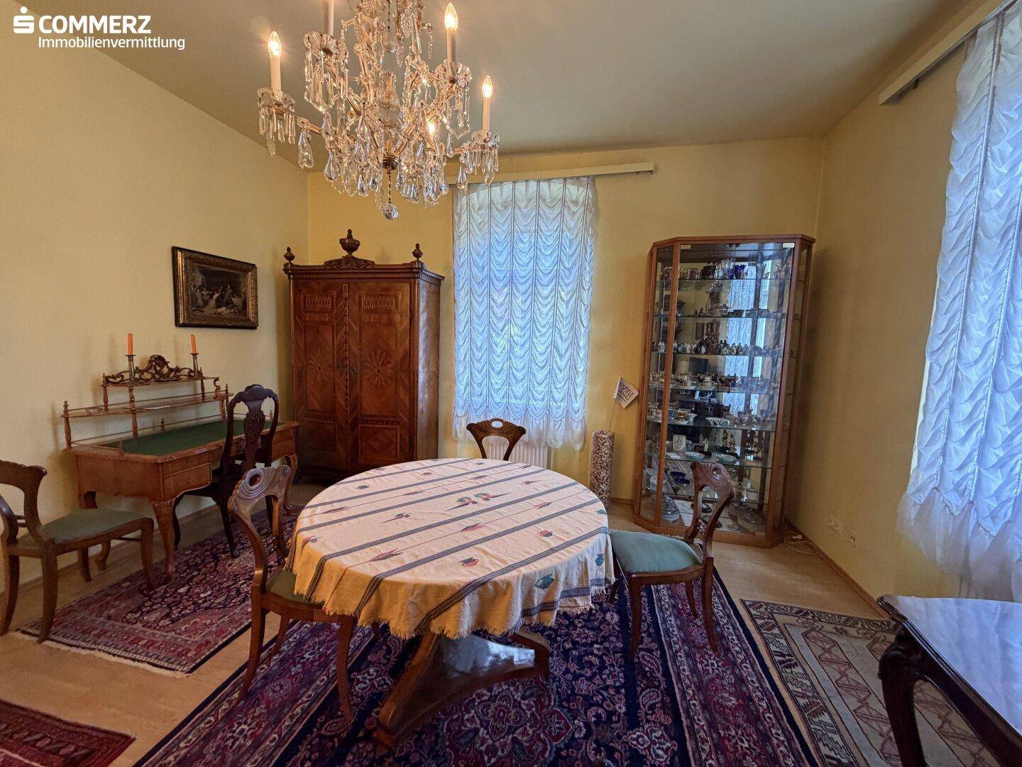 Elegantes Esszimmer mit antikem Mobiliar, Kronleuchter und gemusterten Teppichen.