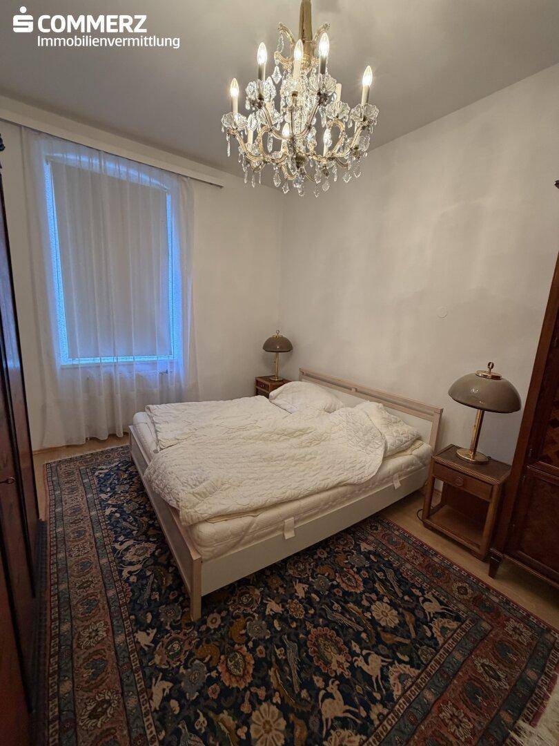 Gemütliches Schlafzimmer mit Doppelbett, Teppich und einem eleganten Kronleuchter.