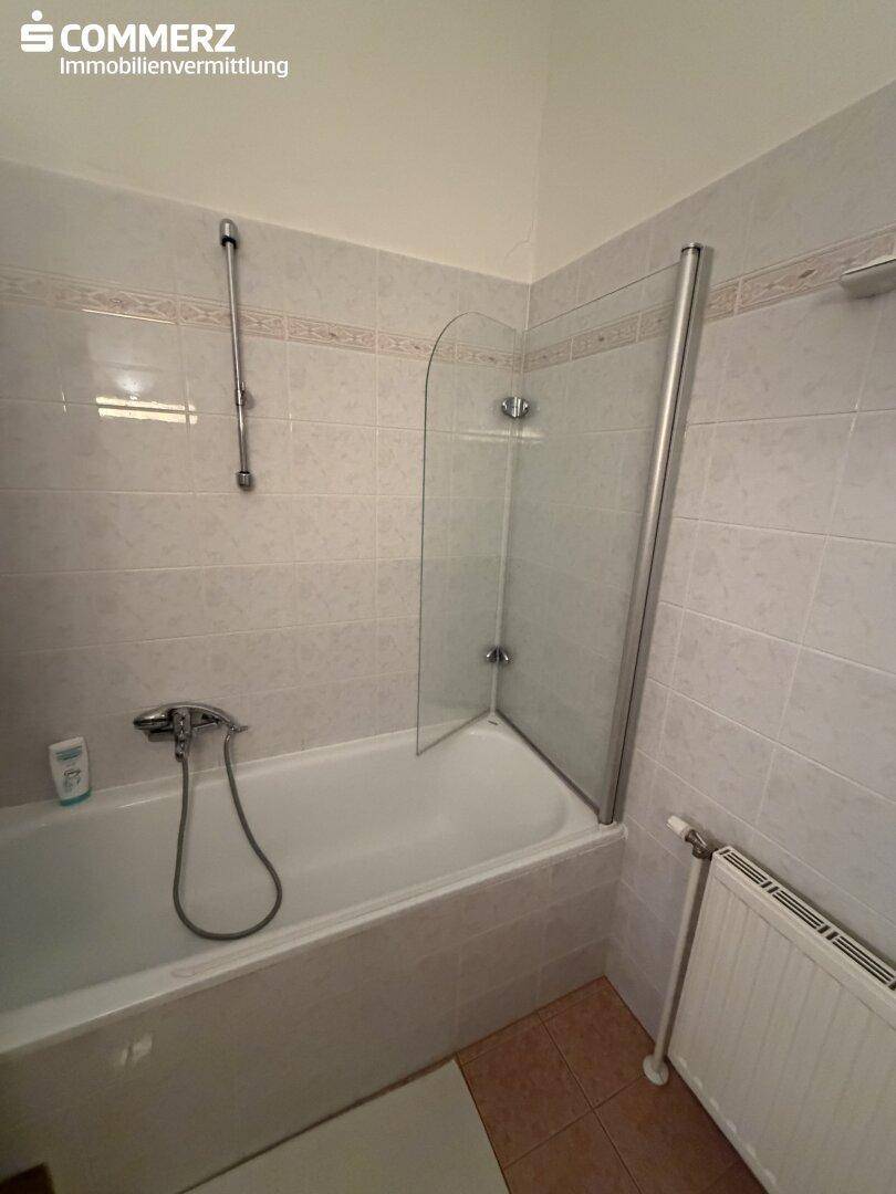 Badezimmer mit Badewanne, Duschabtrennung aus Glas und Heizkörper.
