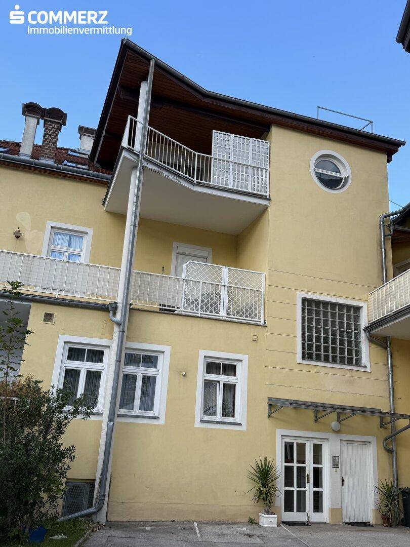 Rückansicht eines Gebäudes mit mehreren Balkonen, Glasbausteinfenstern und gelber Fassade.