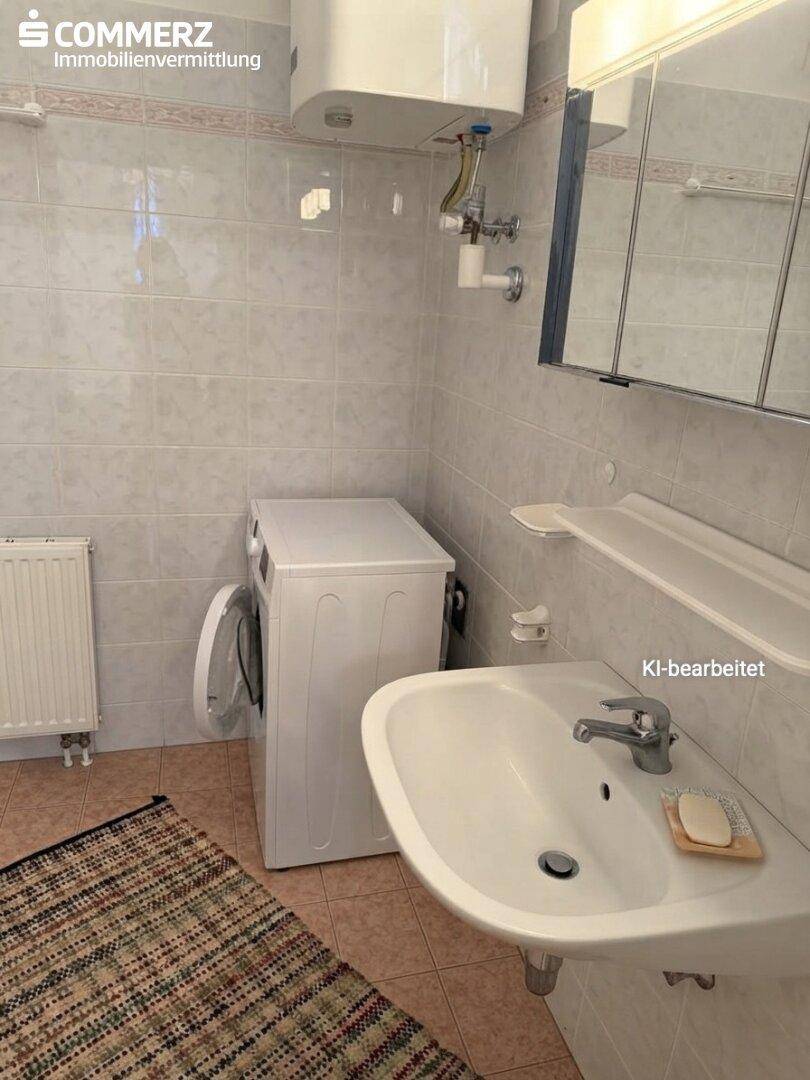 Badezimmer mit Waschbecken, Spiegelschrank, Waschmaschine und hellen Fliesen.