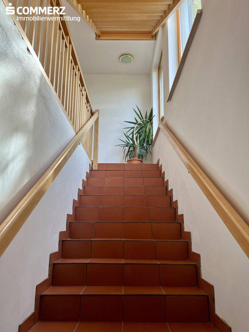 Innenliegende Treppe mit Terrakotta-Fliesen und Holzgeländer, führt in die oberen Etagen.