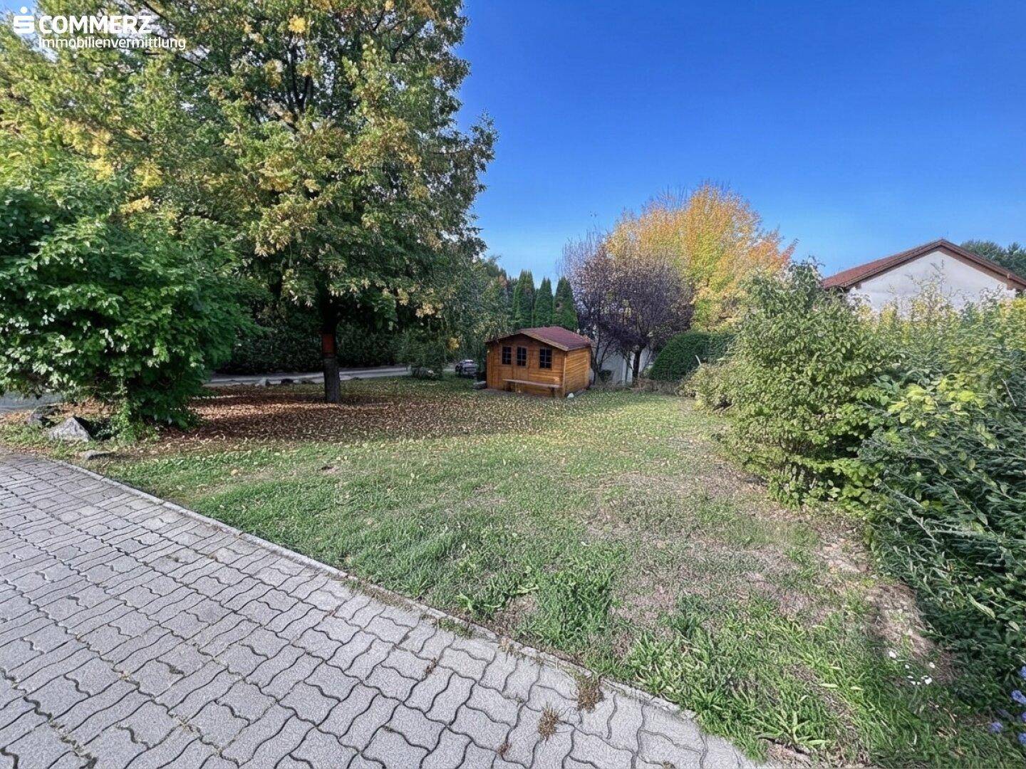 Gepflegter Gartenbereich mit Rasenfläche, Bäumen und einem kleinen Holzschuppen, ideal zum Entspannen.