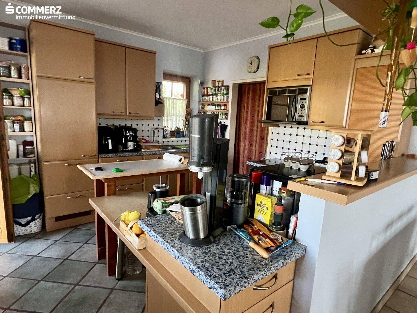 Geräumige Küche mit hellen Holzfronten, gefliestem Boden und viel Arbeitsfläche.