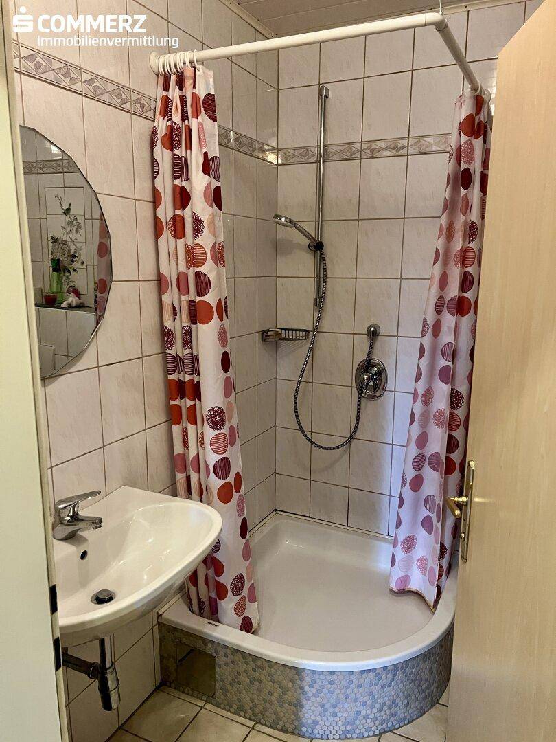 Badezimmer mit Duschkabine, Waschbecken und gefliesten Wänden, funktional eingerichtet.