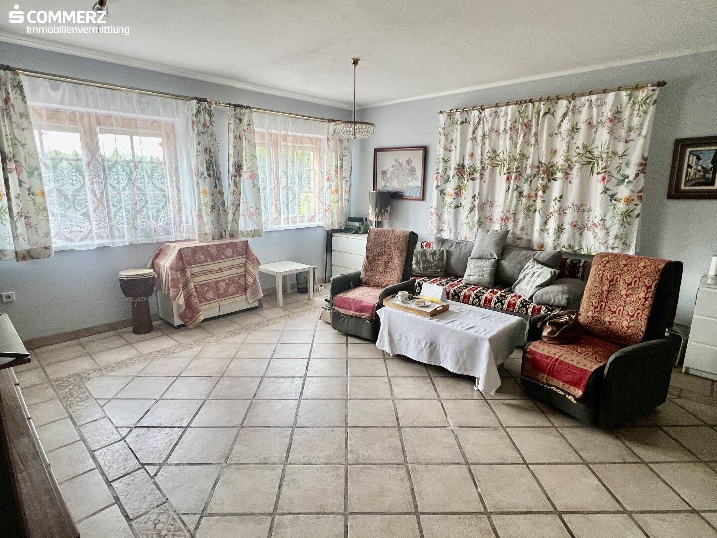 Gemütliches Wohnzimmer mit gefliestem Boden, floralen Vorhängen und traditioneller Einrichtung.
