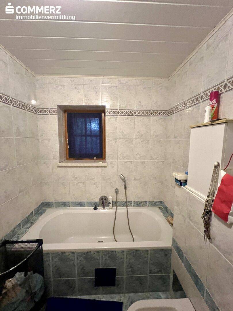 Badezimmer mit Badewanne, gefliesten Wänden und einem Fenster für natürliche Belüftung.